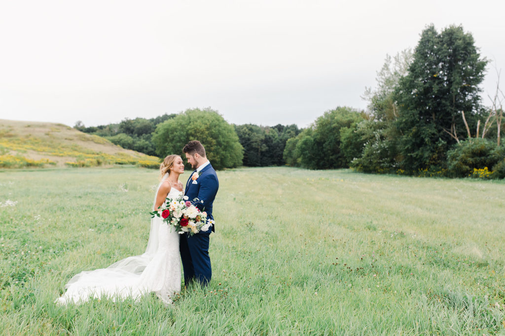 a couple in a field for wedding pictures with a colorful bouquet by Studio Fleurette.